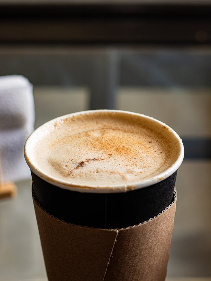 Close-up of a cinnamon-spiced chai latte with foam in a disposable cup, perfect for cozy moments.